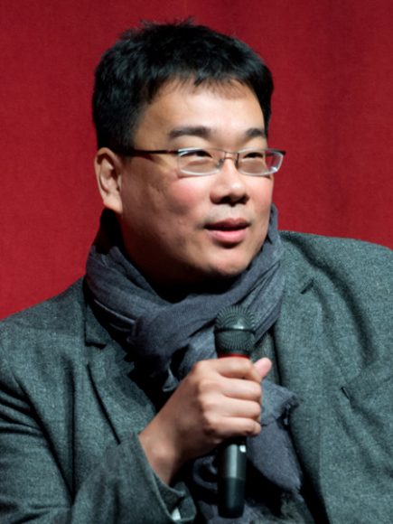 Bong Joon-ho wearing scarf with glasses holding microphone with red background