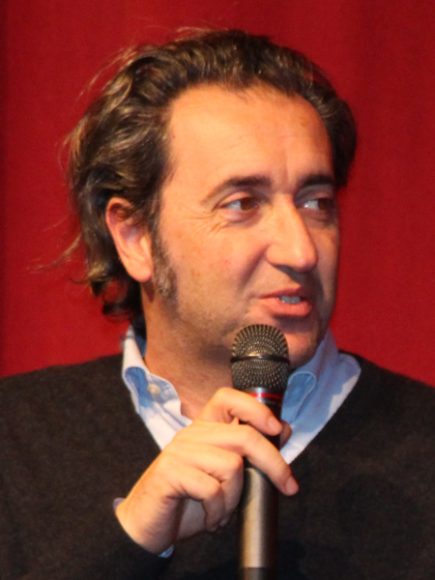 Paolo Sorrentino speaking into microphone on red background