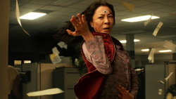 The actress Michelle Yeoh is mid-spin in an office, papers swirl behind her, there's a googly eye on her forehead