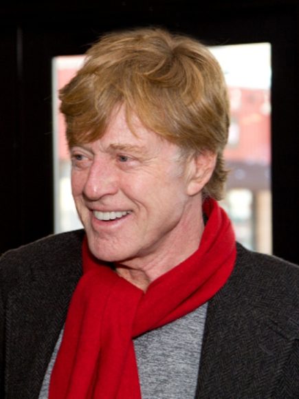 Robert Redford wearing a red scarf, smiling and looking off to his right