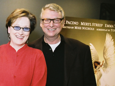 Meryl Streep, wearing a red blouse, laughing next to Mike Nichols who is smiling and wearing a black shirt. Both are wearing glasses.