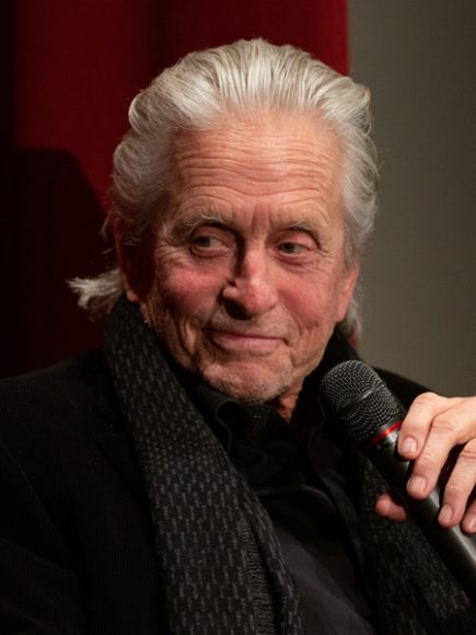 Michael Douglas smiling and holding microphone, looking off outside of frame