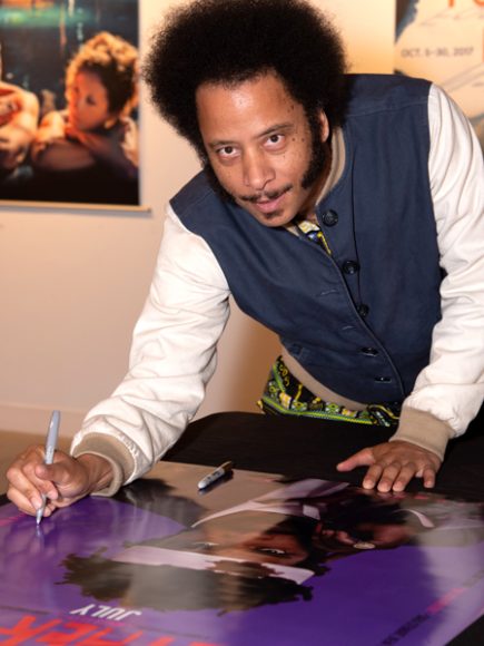 Boots Riley looking into camera, holding pen to sign poster