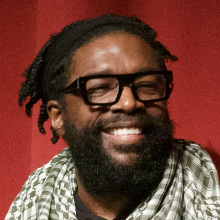 Questlove smiling with glasses in front of red background