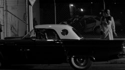 a girl walks home alone at night woman in trenchcoat next to classic car