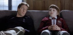 A man (Hugh Grant) and a boy (Nicholas Hault) sit on a couch
