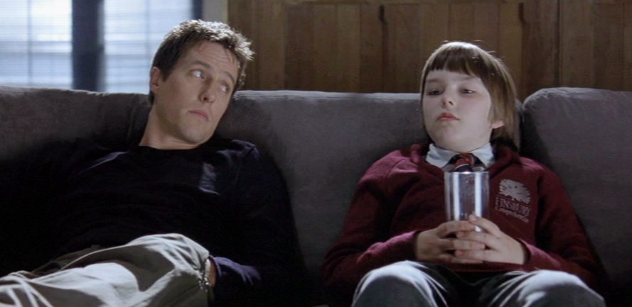 A man (Hugh Grant) and a boy (Nicholas Hault) sit on a couch