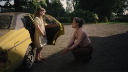A young girl meets a woman outside of a yellow car in THE QUIET GIRL